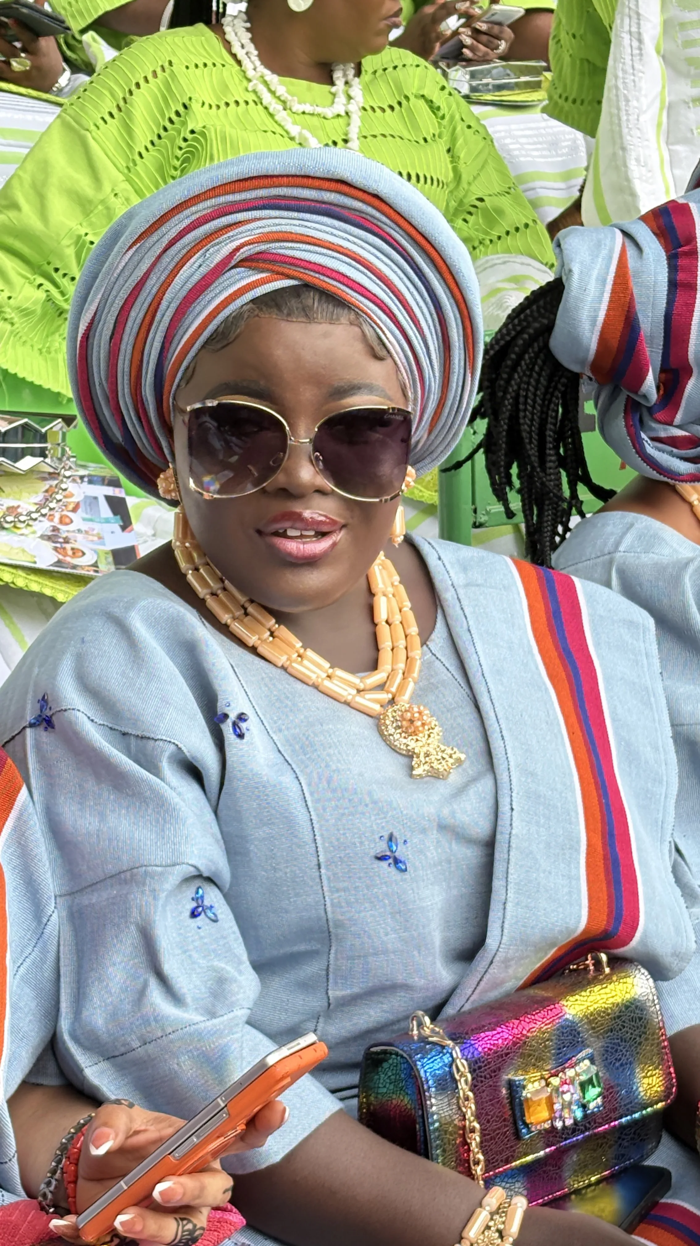Woman in blue aso-oke with gele, sunglasses, beads and a statement purse at Ojude Oba 2026